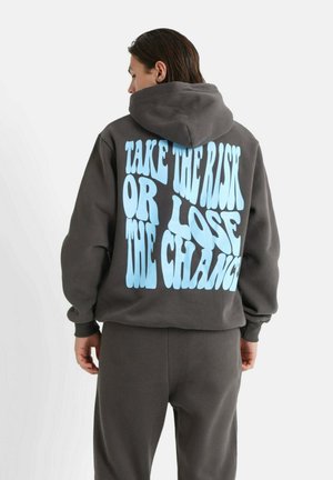 Sudadera gris oscura con un gran texto gráfico azul en la parte posterior. Cuenta con capucha y un corte holgado. Tela suave y puños acanalados.