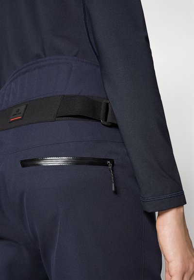 Sinine spordirõivastus, millel on tekstureeritud vöökoht, must reguleeritav rihm ja tõmblukuga tasku, millel on stiilne peegeldav tõmbluku detail.