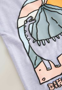 Světlofialová látka s grafikou dinosaura ohraničenou černě. Barvy pozadí zahrnují světle modrou a jemnou broskvovou, s hravým textem dole.