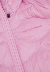 Giacca isolata rosa con design a trapuntatura e cuciture a contrasto. Presenta una cerniera integrale e un logo ricamato "PeakPerformance".
