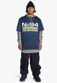 Mörkblå oversized hoodie med grå accenter, stor grafisk text, framficka, matchad med lösa svarta cargobyxor och svarta skor.