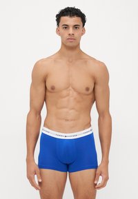 Blauwe katoenen boxershorts met een witte elastische tailleband waarop het "TOMMY HILFIGER" logo in het zwart is afgedrukt. Glad textuur, aansluitend ontwerp.
