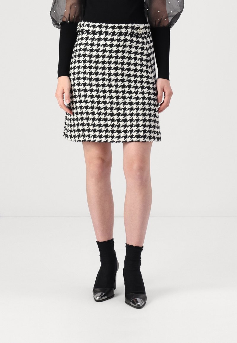 Svart och vit houndstooth-mönstrad kjol, knälång, med åtsittande midja, i kombination med svarta ankelskor och en åtsittande svart topp.