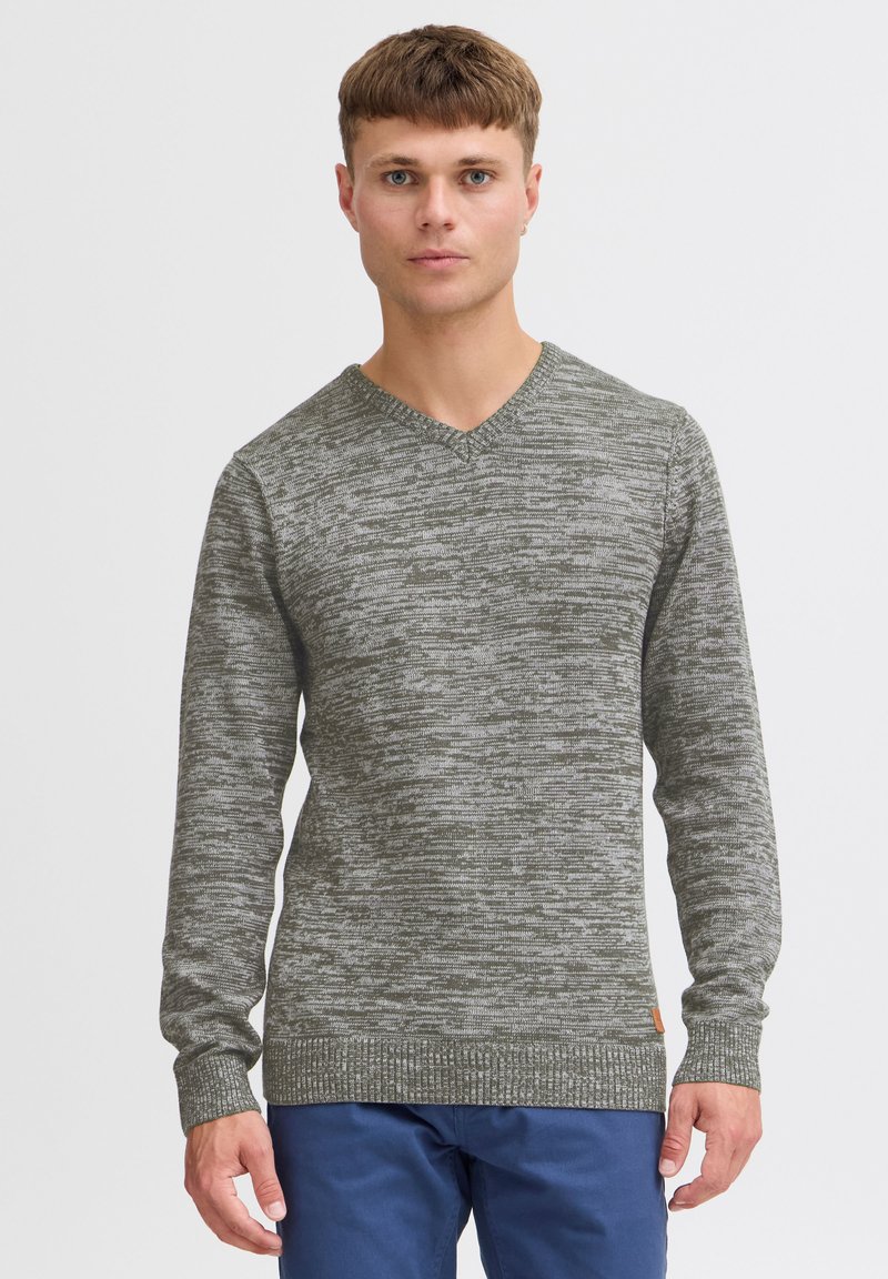Pullover verde a scollo a V con un motivo a maglia testurizzato, con polsini e orlo a costine, realizzato in un materiale morbido, abbinato a pantaloni blu navy.