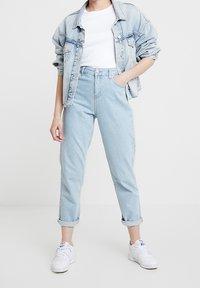 Světle modré denimové džíny s vysokým pasem, ohrnutými manžetami a uvolněným střihem, v kombinaci s bílým tričkem a oversized denimovou bundou.