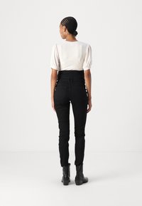 Vaqueros de cintura alta negros combinados con una blusa de manga corta de canalé en un tono beige claro; la modelo lleva botas negras hasta el tobillo. Textura suave, diseño ajustado.