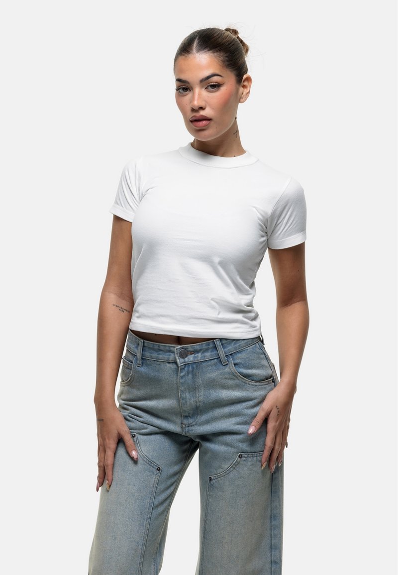 T-shirt bianco aderente a maniche corte con scollo rotondo, abbinato a jeans in denim leggeri a vita alta con tasche e una vestibilità morbida.