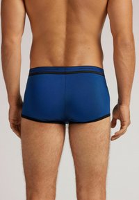 Modré bavlněné boxerky s černým elastickým pasem. Tkanina vypadá hladce, ukazuje těsný střih a minimalistický design.