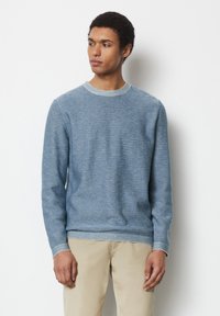 Blauer gestrickter Pullover mit Rundhalsausschnitt, der ein strukturiertes Muster und gerippte Bündchen aufweist. Kombiniert mit beigen Hosen.