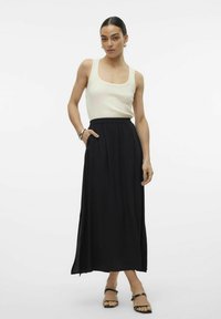 Gonna maxi nera con vita elastica, abbinata a una canotta a coste color crema. La gonna presenta tasche laterali e un design fluido.