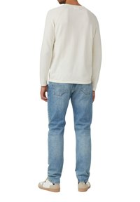 Hellbeiges Langarmshirt mit rundem Ausschnitt, kombiniert mit hellblauen Jeans. Die Sneakers sind in Beige und Weiß gehalten.