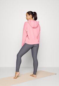 Sweatshirt rosa com capuz combinado com leggings cinzas, exibido sobre um tapete nu. O sweatshirt apresenta um corte relaxado e uma textura suave.