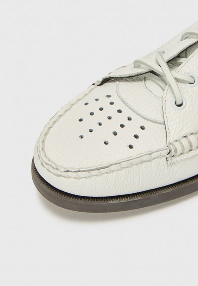Scarpa bianca in pelle con design perforato sulla punta, suola in gomma grigia e lacci grigio chiaro. Presenta bordi cuciti e piccoli accenti circolari.