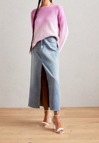 Roze ombre geribbelde trui gecombineerd met een lichtblauwe denim rok met een voorkap. Geaccentueerd met witte gespsandalen.