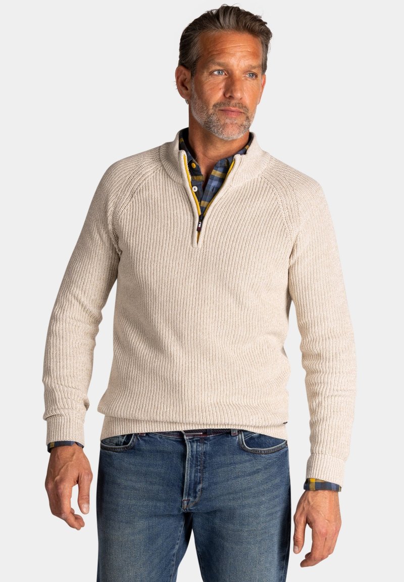 Beige geribbelde gebreide trui met een kwart-rits kraag. Heeft raglanmouwen en een gestructureerde afwerking, gelegd over een blauw geruit overhemd.