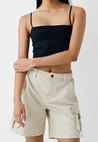 Svart, åtsittande spaghettiärmstopp i kombination med ljusbeige cargoshorts med framfickor och en ficka med dragkedja på sidan.