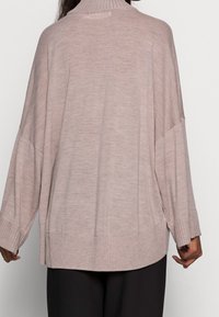 Hellrosa übergroßer Pullover mit hohem, geripptem Kragen, fallenden Schultern und gerippten Bündchen, mit einem strukturierten Strickmuster.