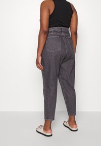 Tmavě šedé džíny s vysokým pasem a zúženými nohavicemi. Mají tradiční zadní kapsy a prošívané švy. V kombinaci se světle zbarvenými nazouvacími botami.