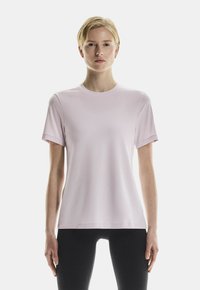 Helles rosa Kurzarmshirt mit Rundhalsausschnitt, aus glattem Material gefertigt, mit einer lockeren Passform und minimalen Nähten. Dazu werden schwarze Leggings getragen.