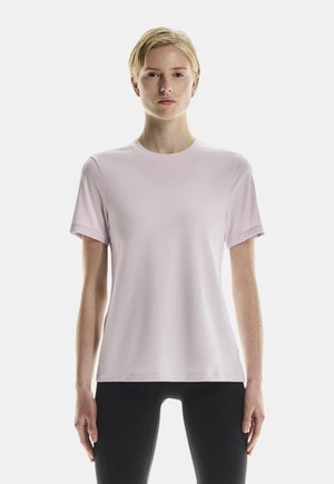 Chemise rose clair à manches courtes avec un col rond, fabriquée en tissu lisse, présentant une coupe décontractée et des coutures minimales. Des leggings noirs sont portés.