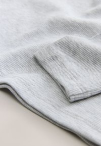 Light gray ribbed fabric with soft texture, featuring a folded cuff and smooth stitching along the edges. Compact and close-up view.