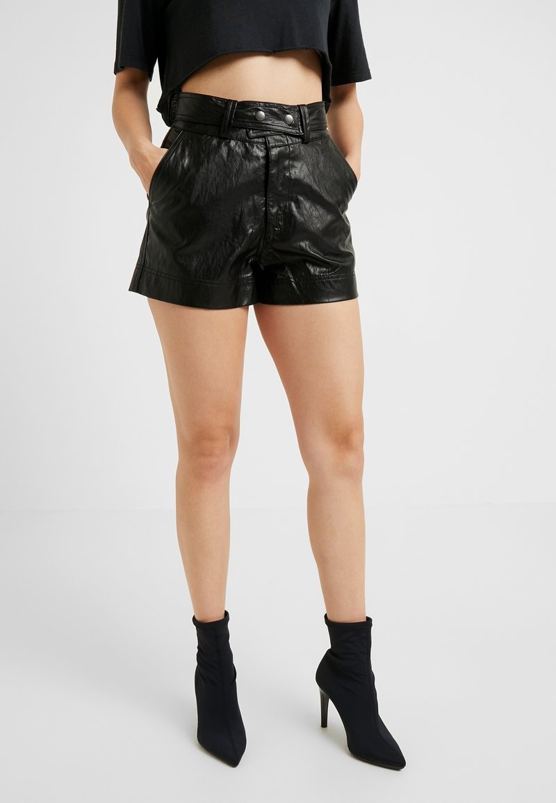 Svarta shorts i konstläder med hög midja, försedda med två sidofickor och en slät, glänsande yta. Tillsammans med svarta ankle boots i sockmodell.