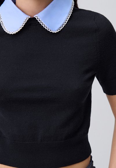 Suéter negro de manga corta con un cuello azul claro que presenta un borde decorativo blanco, confeccionado en una suave tela de punto.