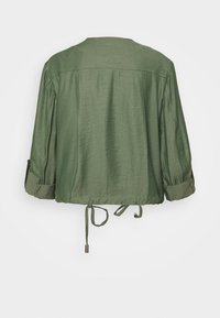 Zielona krótka kurtka z podwiniętymi rękawami 3/4 i regulowanym sznurkiem u dołu, przedstawiona z tyłu na białym tle.