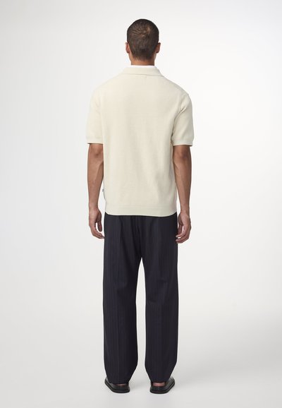 Korte ærmer, cremefarvet strikket polo-shirt med et struktureret mønster, parret med højtaljede, mørke stribede bukser.