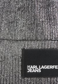 Crna i srebrna rebrasta tkanina s teksturiranom površinom. Sadrži crnu oznaku s bijelim tekstom "KARL LAGERFELD JEANS."