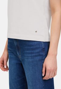 Haut blanc à manches courtes avec un subtil accent argenté à l'ourlet, associé à un jean bleu avec un design classique à cinq poches.