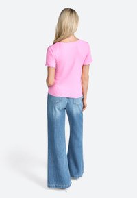 T-shirt rose clair à rayures avec des manches courtes à volants, associée à un jean large bleu clair. Coutures visibles et détails de texture douce.