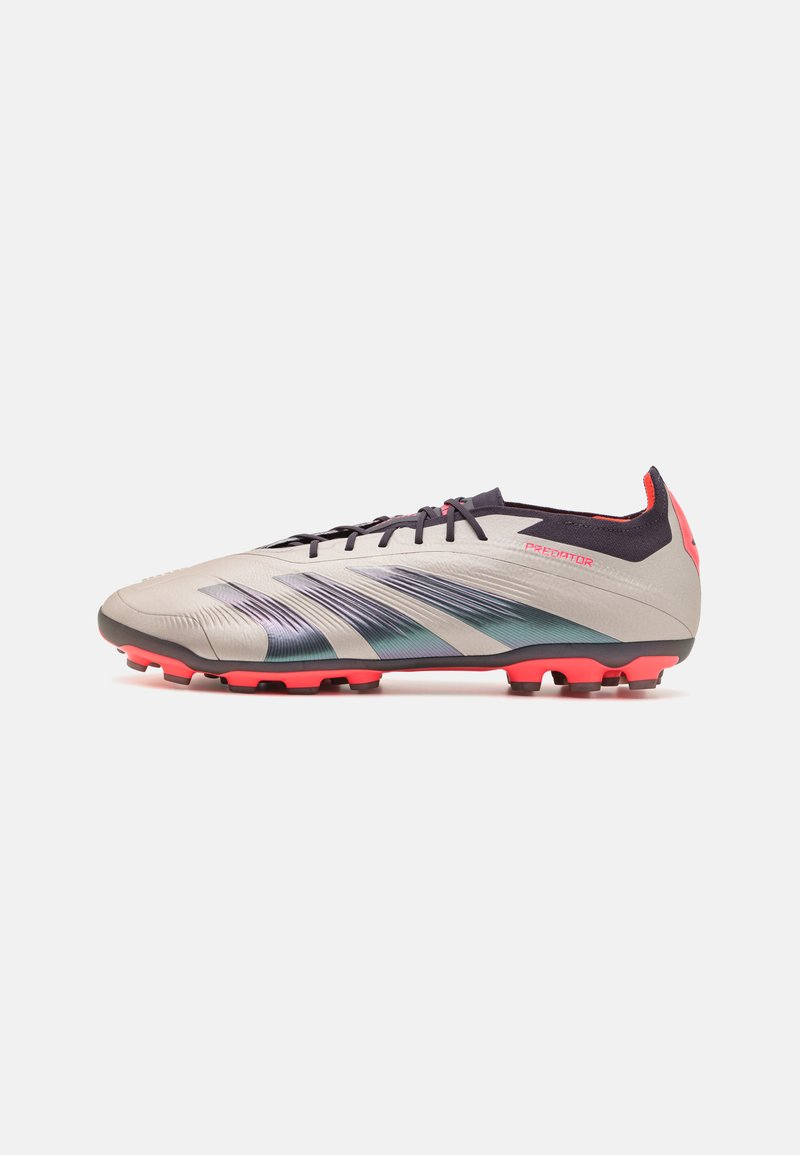 Crampon de football avec un dessus gris, présentant des rayures bleu irisé. Lacets noirs, accents roses et surface texturée. Semelle à crampons pour une meilleure traction.