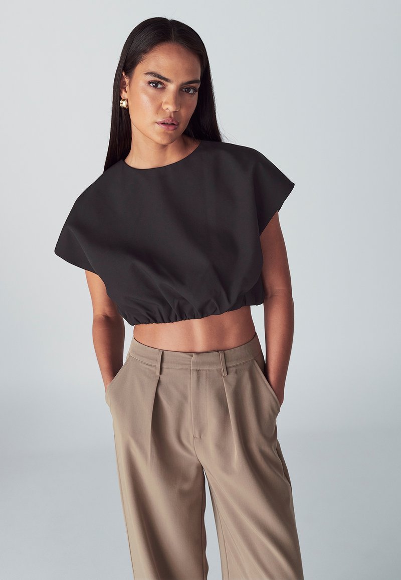 Černý croptop s krátkými rukávy a nařaseným lemem, kombinovaný s béžovými kalhotami s vysokým pasem, které mají sklady a boční kapsy.