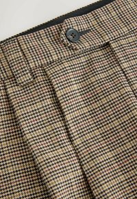 Villasegu houndstooth-mustriga püksid, mis sisaldavad beeži, pruunide ja mustade toone. Sisaldab ees pleati ja sinist nööbi detaili.