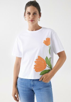 Camiseta blanca de manga corta con un diseño de flores naranjas en el lado izquierdo, fabricada en algodón, con un ajuste holgado y cuello redondo.
