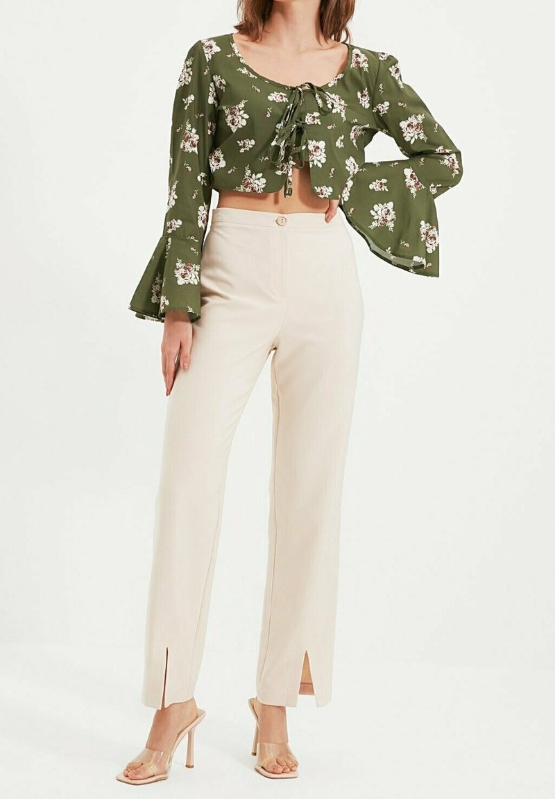 Haut court fleuri vert avec manches évasées, assorti à un pantalon taille haute crème avec fermeture à boutons et fentes latérales ; sandales à talons transparents.