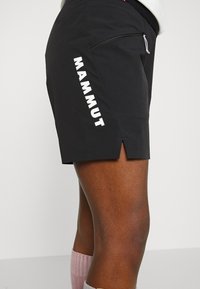 Black shorts made of stretch fabric, featuring a side zipper pocket and a white "MAMMUT" logo. Shorts have side slits for ease of movement.