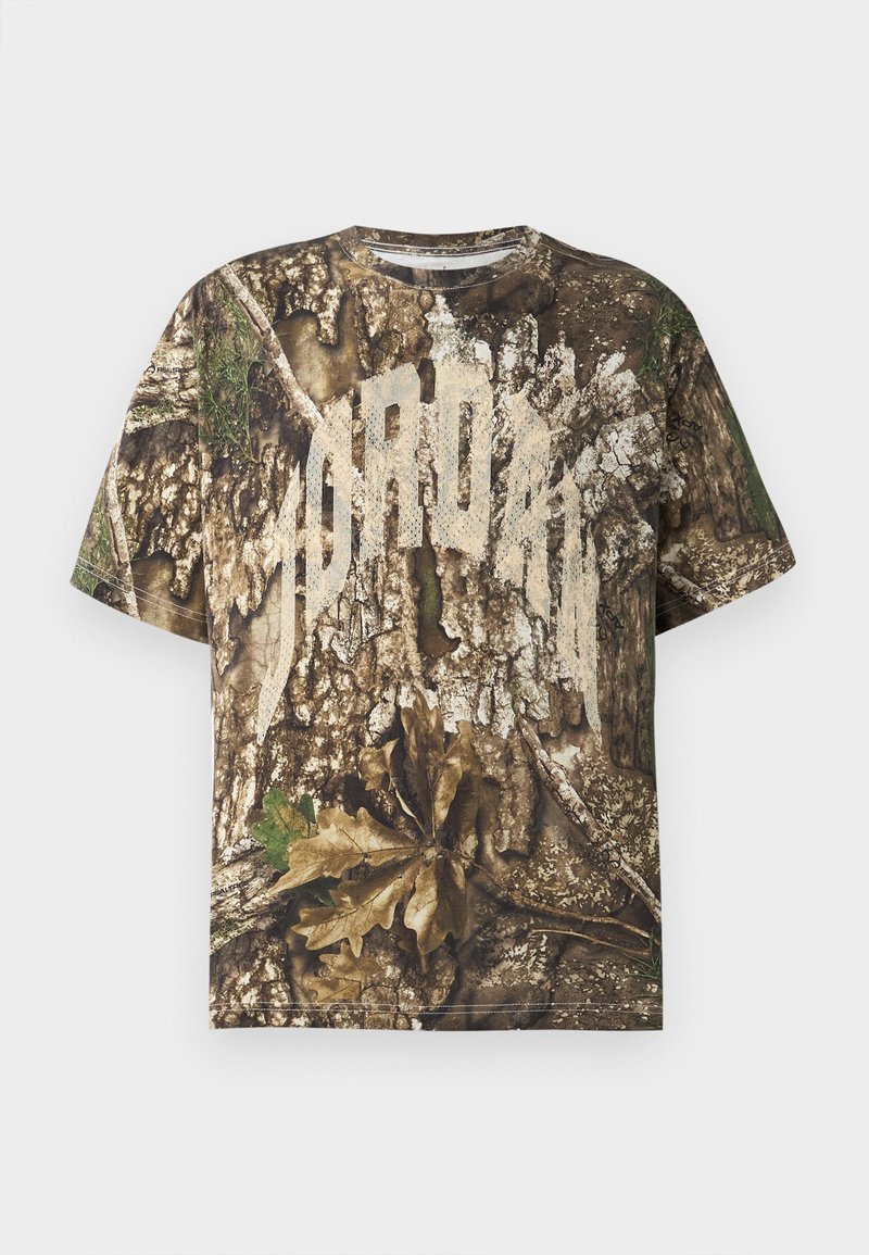 T-shirt à manches courtes avec un imprimé camouflage réaliste d'écorce d'arbre et de feuilles, et un grand texte blanc décoloré à travers la poitrine.