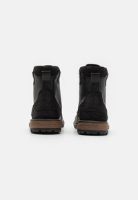 Černé kožené kotníkové boty s matným povrchem, které mají hnědou texturovanou podrážku a poutko na zadní straně pro snadné obouvání.