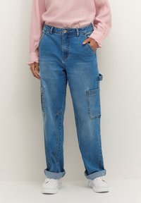 Blå denim cargobyxor med avslappnad passform, med sidofickor, uppvikta fållar och knäppning, i kombination med en ljusrosa topp.