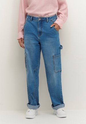 Pantaloni cargo in denim blu con vestibilità rilassata, caratterizzati da tasche laterali, orli arrotolati e chiusura a bottone, abbinati a una maglia rosa chiaro.