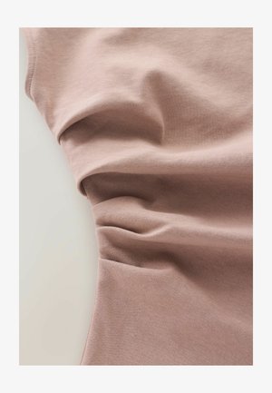 Lichtroze stof, zachte textuur met soepele plooien, met een lichte glans. Het materiaal lijkt rekbaar en lichtgewicht, ideaal voor casual kleding.