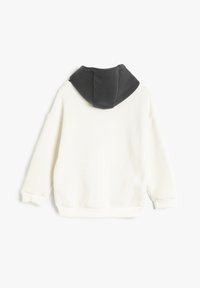 Vaalean beige huppari, jossa on musta huppu, pitkät hihnat ja ribbireunat. Pehmeä materiaali, rento leikkaus ja minimimuotoilun yksityiskohdat.