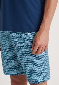 Blauwe t-shirt gecombineerd met patroon zwemshorts in aqua tinten, met verticale langwerpige vormen in donkerblauw en witte accenten.