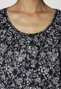 Blusa floral navy con cuello redondo, detalle fruncido y patrones florales plateados en una tela ligera.