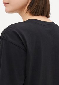 Svart t-shirt med kort ärm och rund halsringning, tillverkad i mjuk bomull. Tyget verkar slätt med en avslappnad passform och minimala sömdetaljer.
