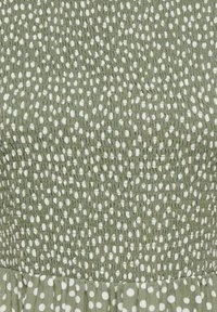 Close-up van groen stof met geplooide textuur en onregelmatig patroon van witte stippen dat overgaat in grotere witte stippen op geplooide stof.