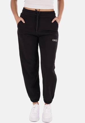 Pantaloni della tuta neri con polsini elasticizzati, vita con cordino e tasche frontali; presenta un testo ricamato bianco sull'anca sinistra. Abbinati a sneakers bianche.