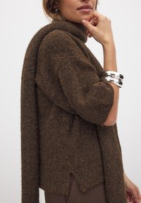 Brauner, strukturierter Strickpullover mit kurzen Ärmeln, hohem Halsausschnitt und seitlichem Schlitz. Enthält ein passendes, drapiertes Schal-Accessoire.
